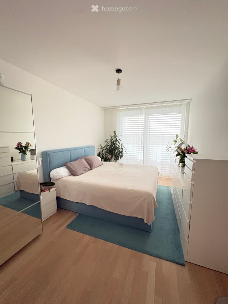 A modern bedroom with a large bed, nightstands, a mirror, and potted plants near the window.