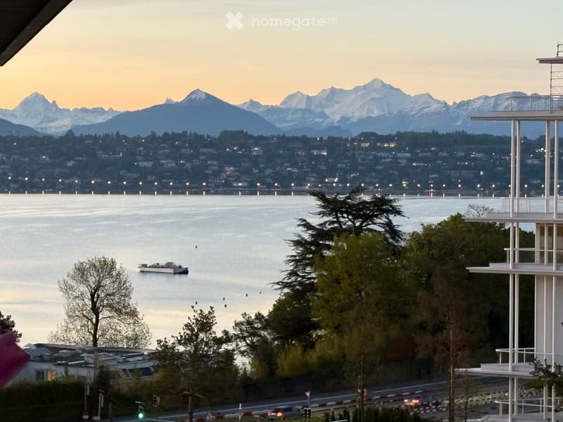 View of a waterfront with mountains in the background, a calm body of water, and a distant cityscape.