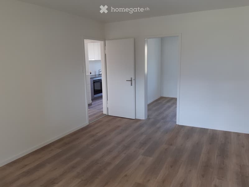 Empty room with wooden flooring and white walls, featuring two open doors leading to adjacent spaces.