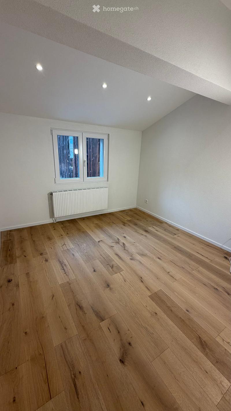 Empty room with wooden flooring, white walls, and a window with double glass panels. A radiator is mounted on the wall below the window.
