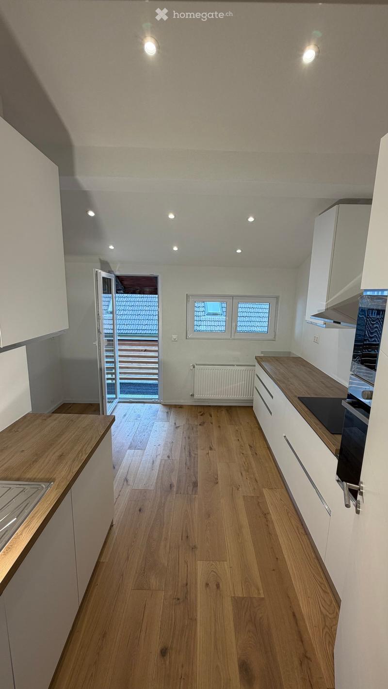 Modern kitchen with light wooden flooring, white cabinets, wooden countertops, and an open door leading to a balcony area.