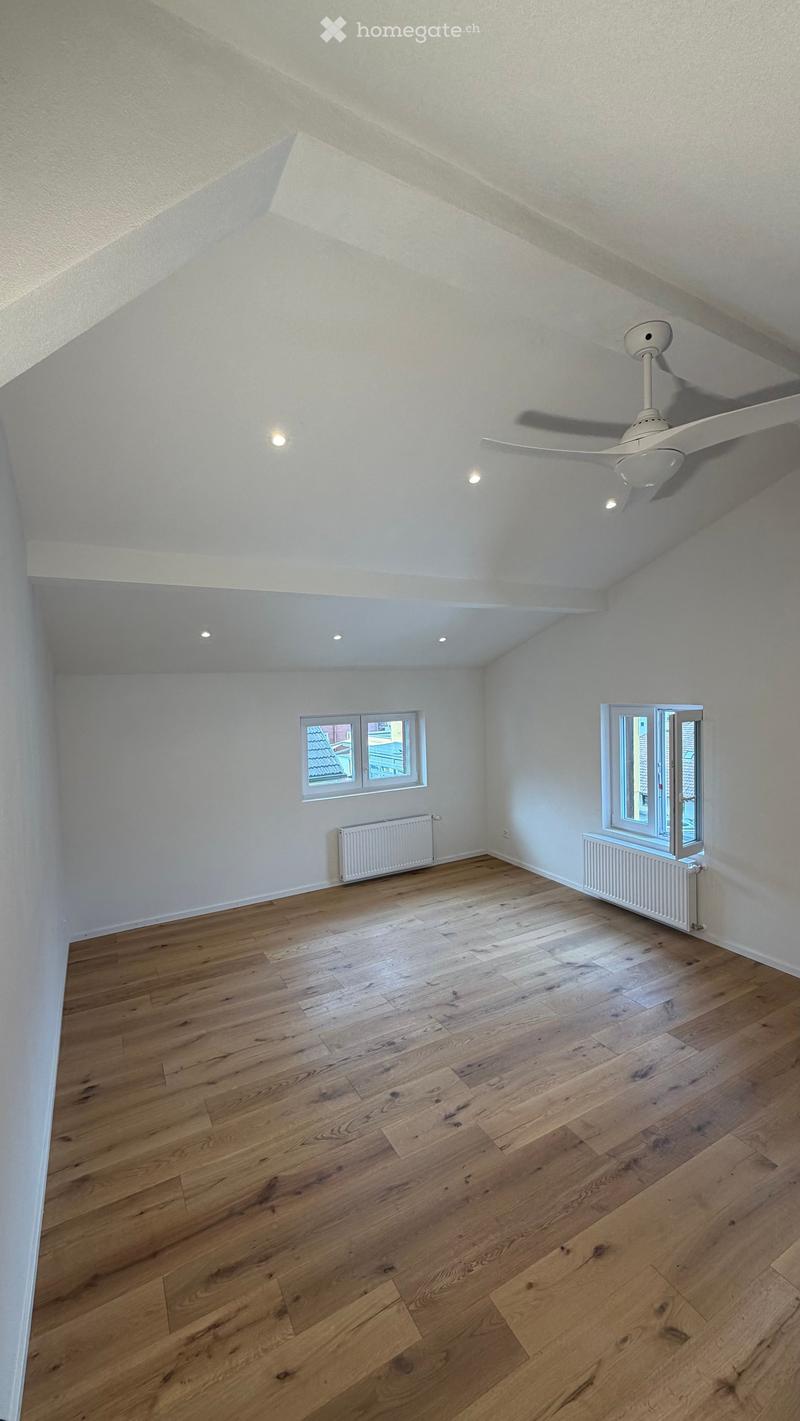 Empty room with wooden flooring, white walls, and a ceiling fan. Two windows provide natural light, and radiators are installed under the windows.