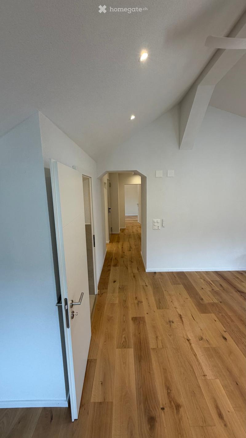 Empty hallway with wooden flooring, white walls, and recessed lighting. Features an open doorway leading to another room.