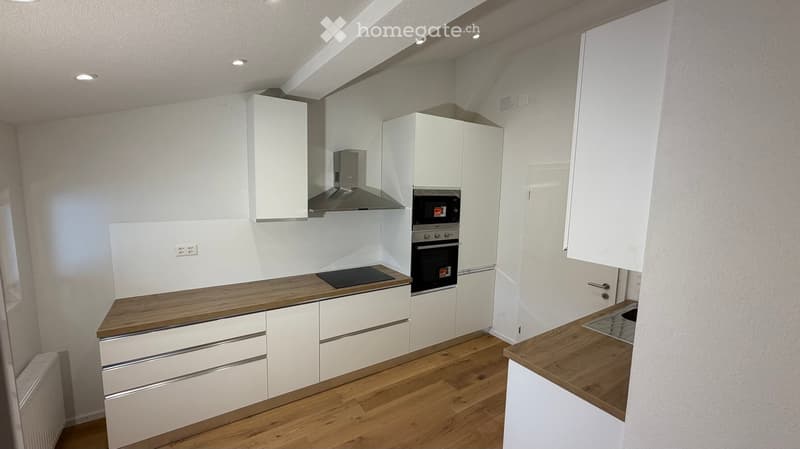 Modern kitchen with white cabinets, wooden countertops, and stainless steel appliances including a stove, oven, and range hood.