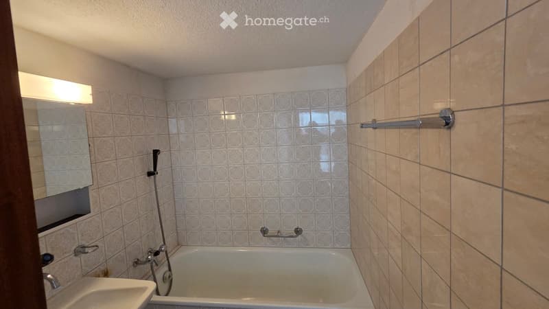 Bathroom with a bathtub, sink, mirror, and tiled walls. Features a showerhead and handrail for accessibility.