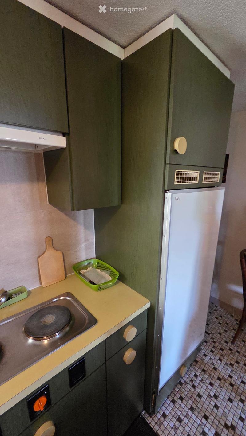 Compact kitchen with green cabinets, a white refrigerator, a stove, a sink, and a cutting board on the counter.
