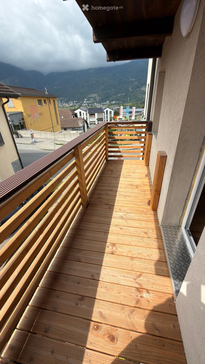 Wooden balcony with railing, overlooking a town and mountains.