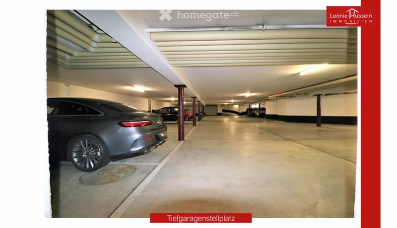 Underground parking area with several parked cars, concrete floor, white ceiling, and red support pillars.
