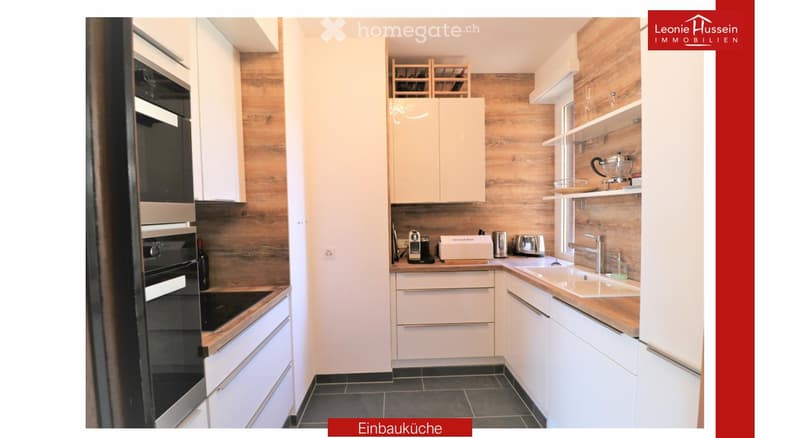 Modern kitchen with white cabinets, wooden accents, stainless steel appliances, and a built-in oven. Features a sink with a modern faucet, shelves, and various small appliances.
