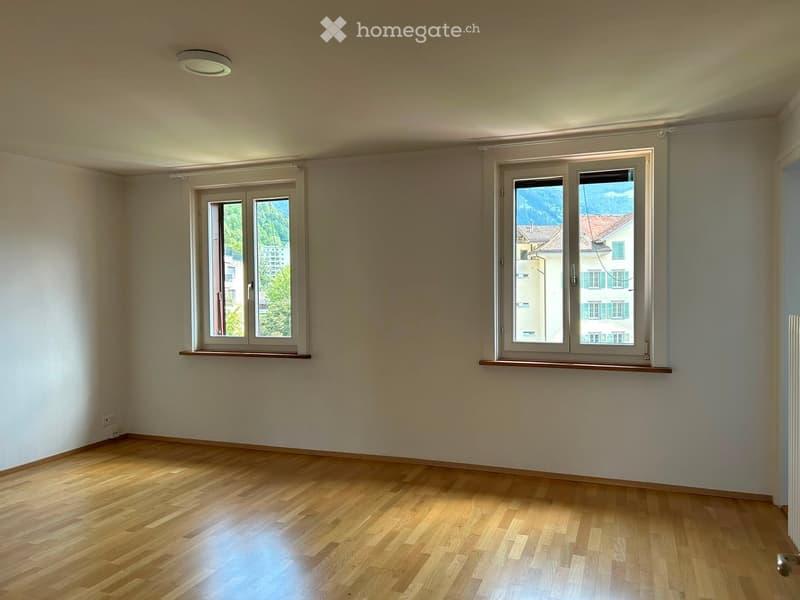 Empty room with wooden flooring, white walls, and two windows offering a view of the outside. The room has a simple, clean design with no furniture or decorations.
