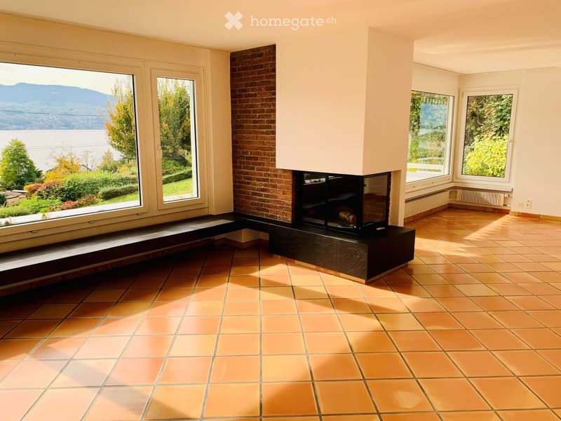 Living Room. Bright living room with terracotta tiled floor, large windows offering scenic views, and a central brick fireplace.