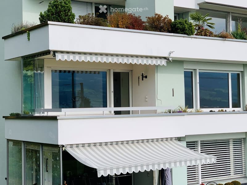 Building. Modern multi-story building with white balconies, striped awnings, and greenery on the rooftop.