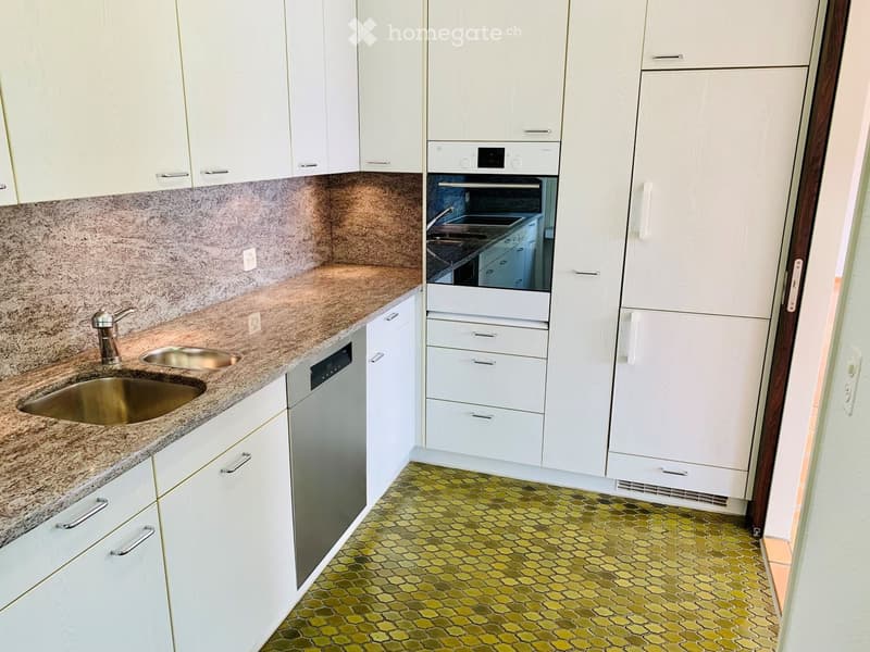 Kitchen. Modern kitchen with white cabinets, granite countertops, stainless steel sink and faucet, dishwasher, oven, and refrigerator. Green hexagonal tile floor.