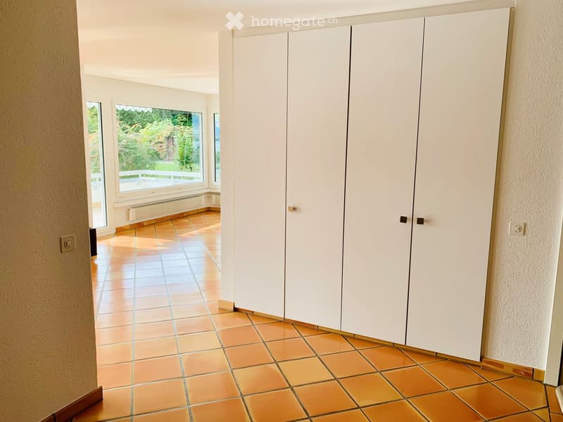 Unfurnished Room. Empty room with tiled floor, white built-in closet, large window with view of greenery, and radiator under the window.