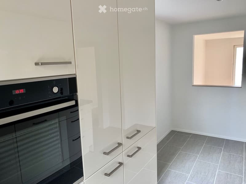 Modern kitchen with white cabinets, stainless steel oven, and tiled floor.