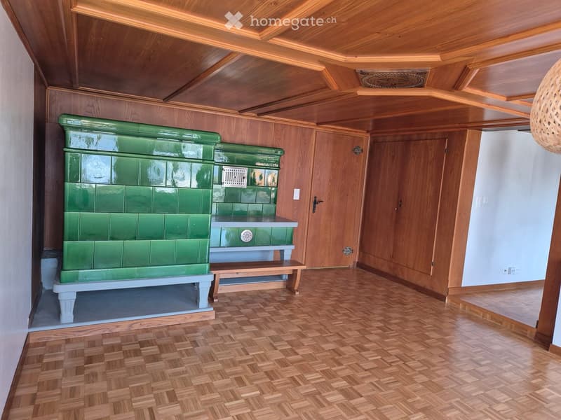 Room with wooden walls and ceiling, green tiled fireplace, wooden bench, and wooden herringbone flooring.