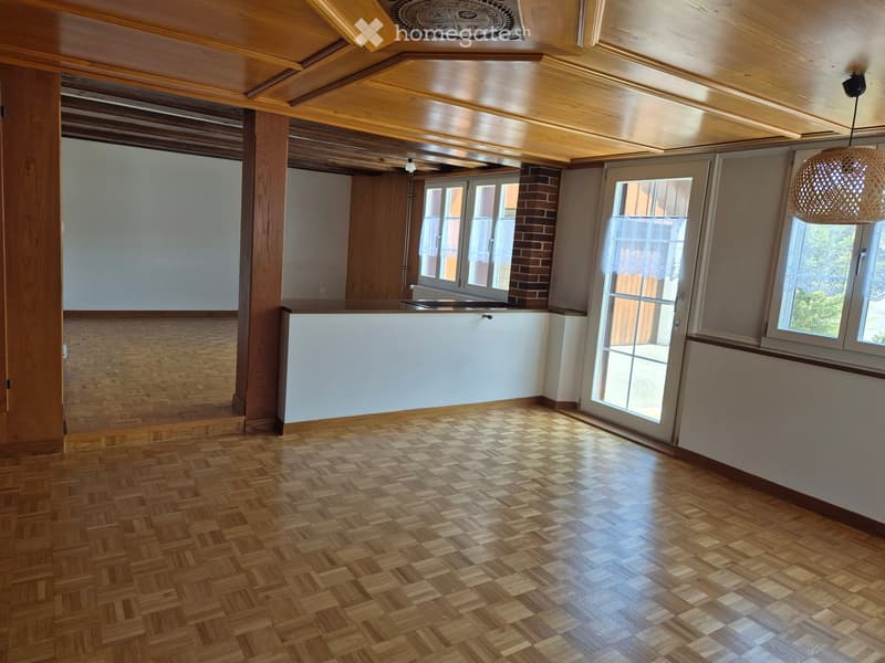 Empty room with wooden herringbone flooring, white walls, large windows, and a white cabinet. The ceiling features exposed wooden beams and a decorative medallion.
