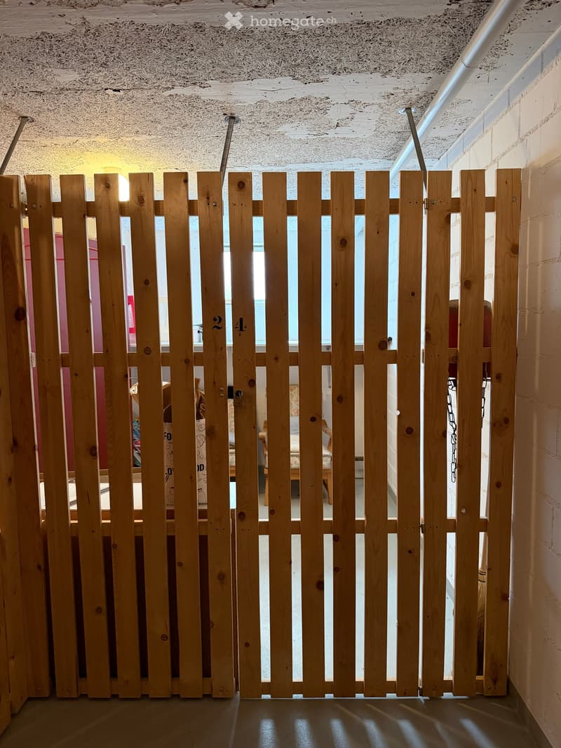 A wooden fence or barrier with vertical slats and numbers "2" and "4" visible, partially obscuring a view into an adjacent room with furniture and decor.