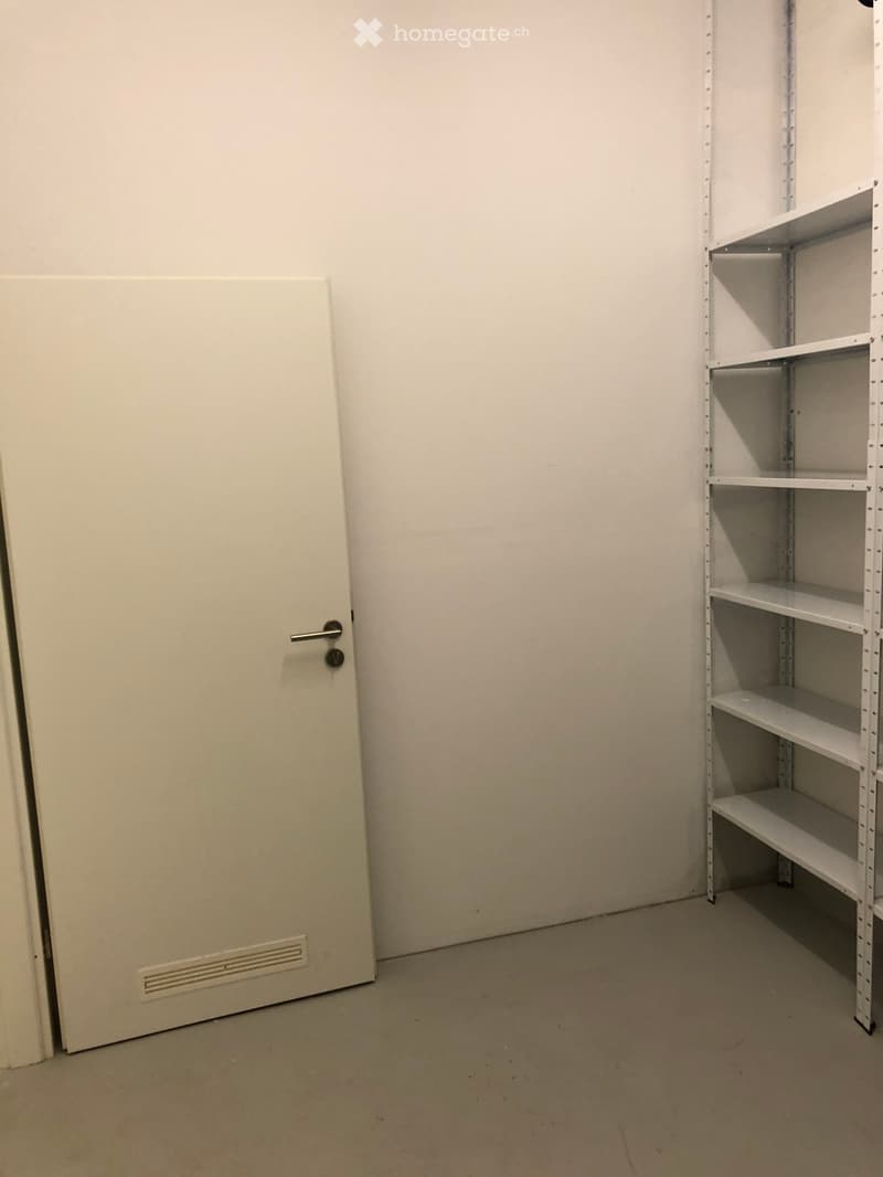 Empty room with white walls, a closed door, and a white shelving unit with multiple empty shelves.