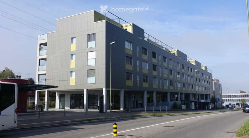Modern multi-story building with grey and yellow facade, large windows, and balconies.
