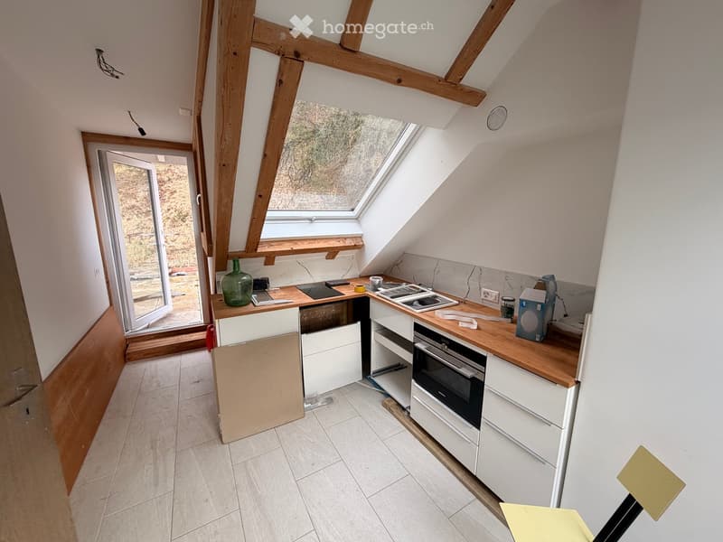 Modern kitchen with white cabinets, wooden countertops, and a built-in oven. Features a skylight and a large window with a view of the outdoors.
