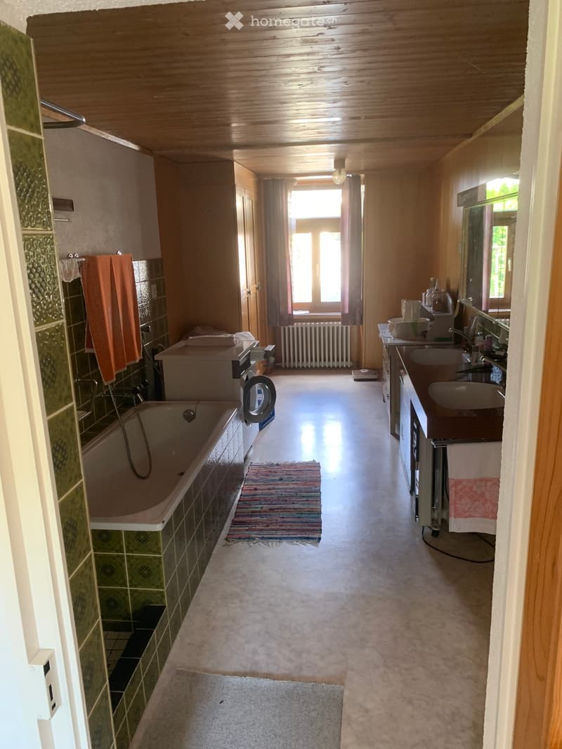 Bathroom with wooden ceiling, bathtub, sink, mirror, towels, washing machine, radiator, and window with curtains.