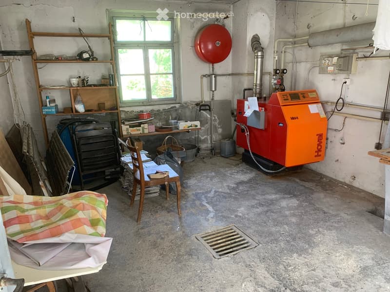 Utility room with concrete floor, wooden shelves, heater, chair, table, and various stored items.