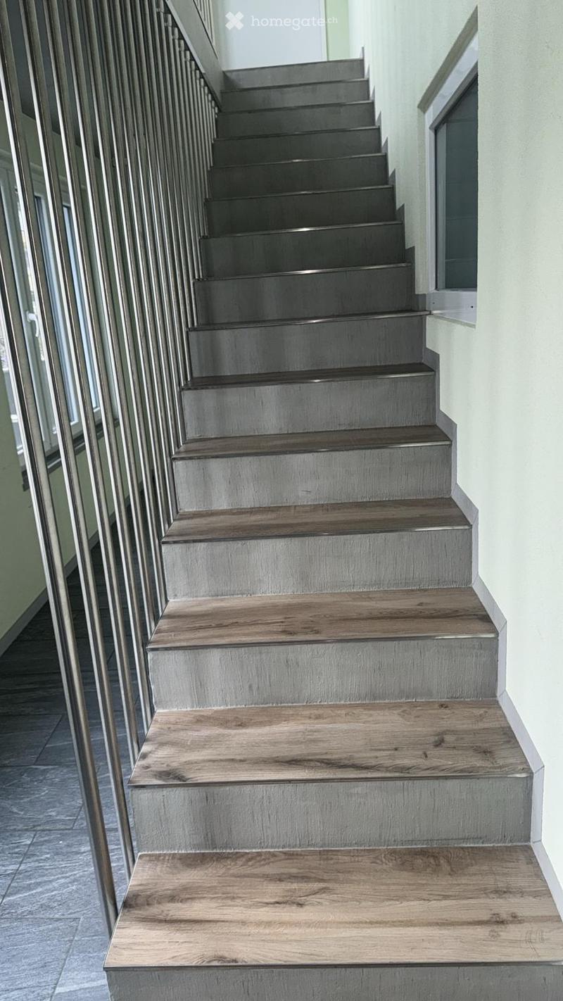 Modern staircase with alternating wood and concrete steps, featuring a sleek metal railing and a clean, contemporary design.