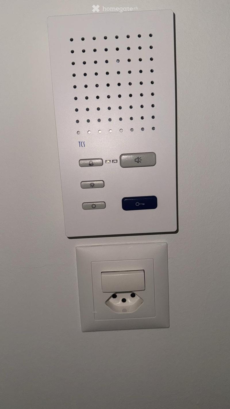 A modern wall-mounted light switch panel with multiple buttons and a standard electrical outlet below it.