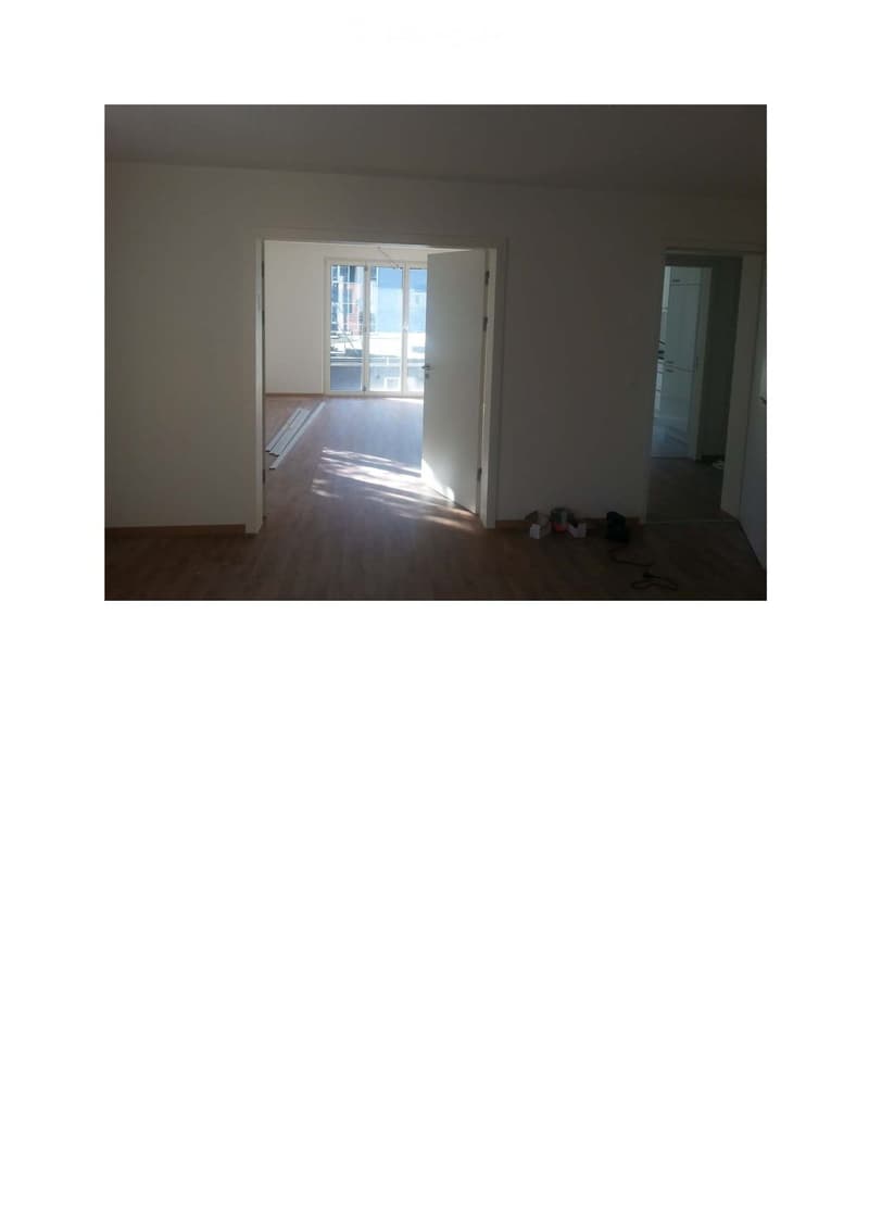 Empty room with wooden flooring, white walls, and open doors leading to other rooms and a balcony area.