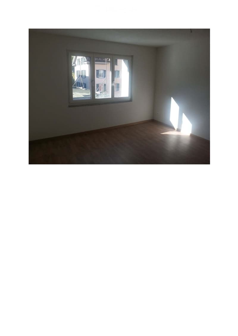Empty room with wooden flooring and a large window letting in natural light. No furniture or equipment is present.