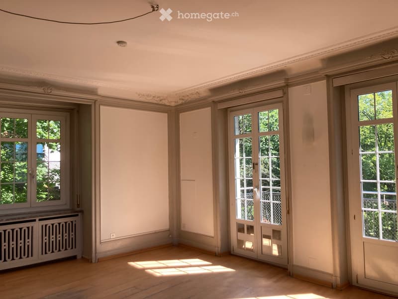 Empty room with wooden flooring, large windows, and ornate ceiling moldings. No furniture or equipment present.