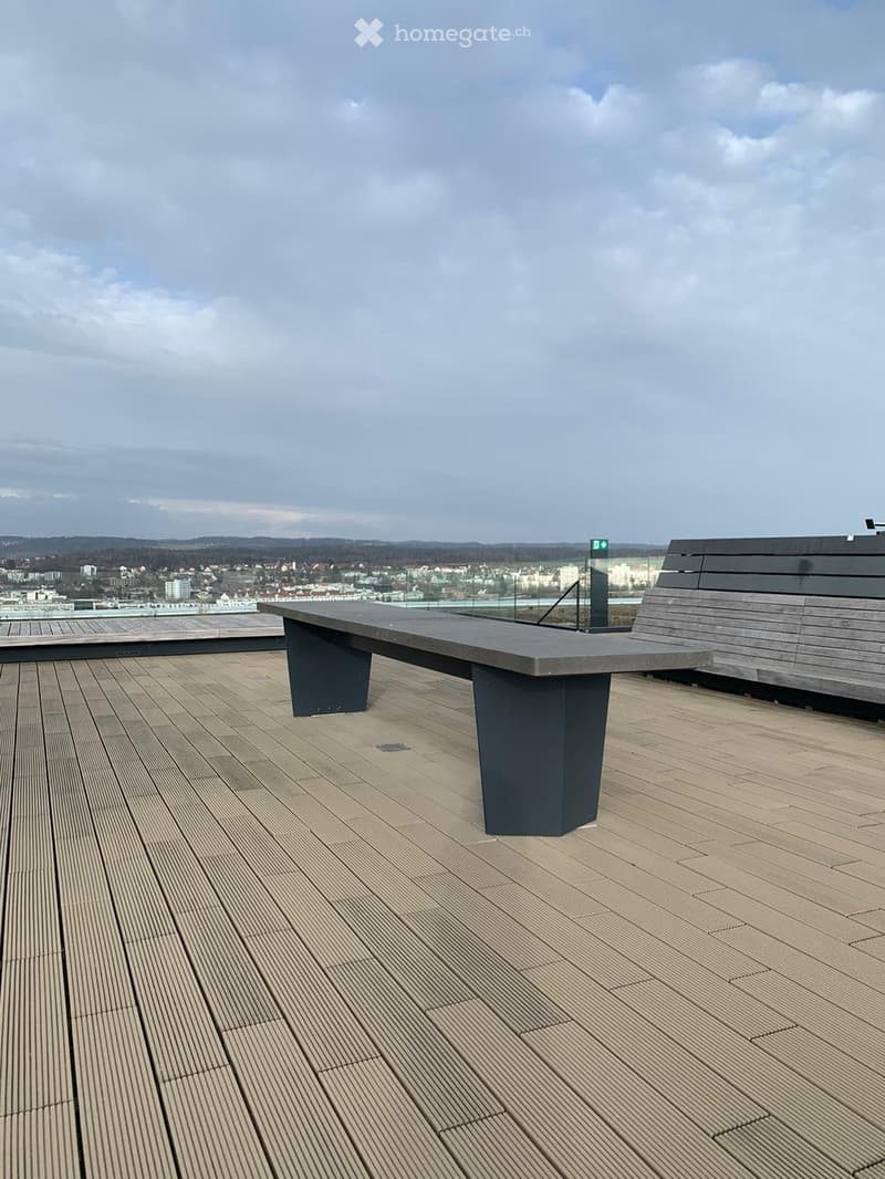 Wooden deck with a black table and bench, overlooking a cityscape.