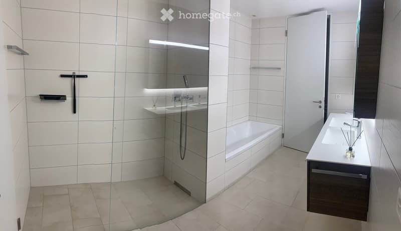 Modern bathroom with a bathtub, double sink, glass shower enclosure, and built-in storage. Features white tiles, sleek fixtures, and a minimalist design.