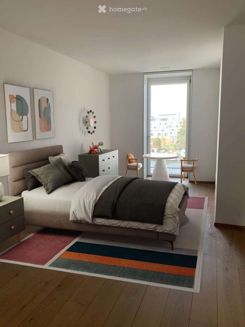 Modern bedroom with a large bed, nightstand, chair, small table, and artwork on the wall. The room features wooden flooring and colorful rugs.
