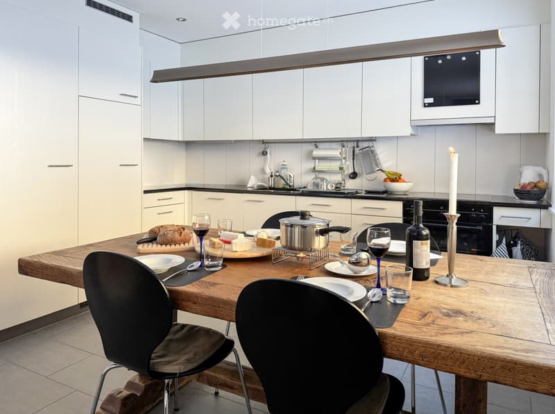 Modern kitchen with white cabinets, a wooden dining table, and various kitchen items including a pot, wine bottle, and candle.