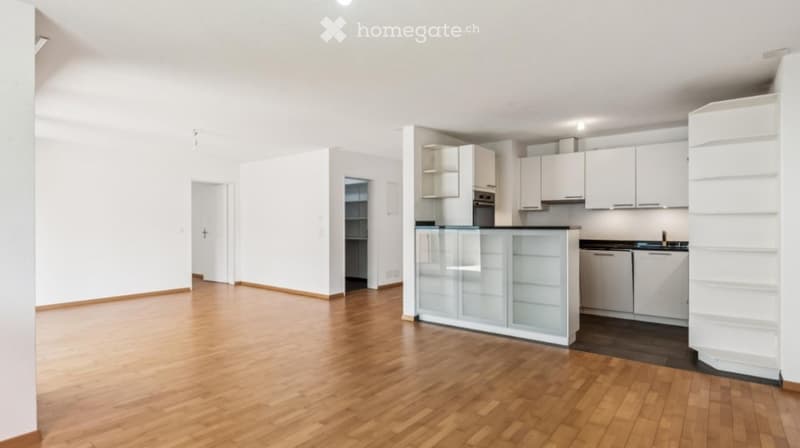 Empty kitchen with white cabinets, a central island, and wooden flooring. No furniture or appliances are present.