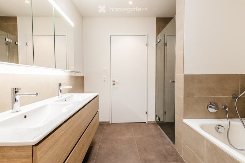 modern bathroom with double sink, large mirror, walk-in shower, bathtub, wooden cabinets