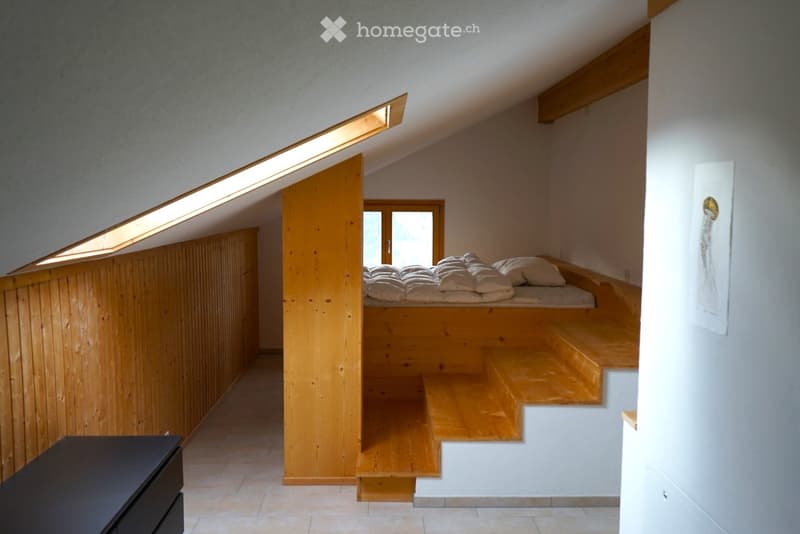 Cozy attic bedroom with wooden bed platform, built-in steps leading to the bed, skylight windows, and a small nightstand.