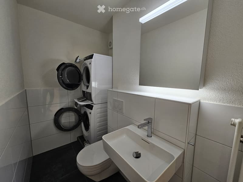 Bathroom with white tile floor, white walls, a toilet, a sink, and a stacked washer and dryer unit.