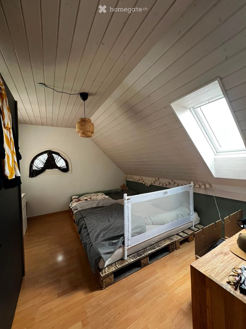 Cozy attic bedroom with wooden floors, slanted wooden ceiling, skylight window, and a bed with a mosquito net.