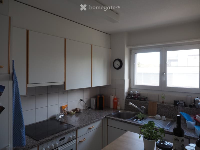 Modern kitchen with white cabinets, granite countertops, and stainless steel appliances. Features include a built-in oven, sink, and various kitchen items on the counter.