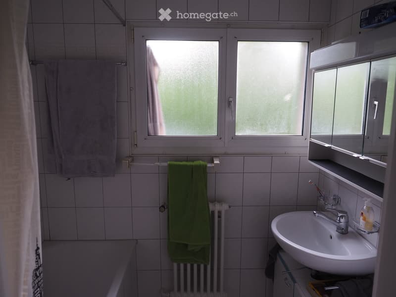 Bathroom with white tiled walls, a sink with a faucet, a mirror cabinet, a radiator, and towels hanging on a rack.