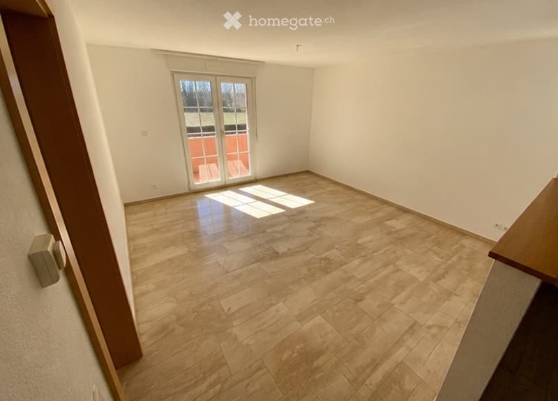 Empty room with wooden flooring, white walls, and a large glass door leading to a patio.