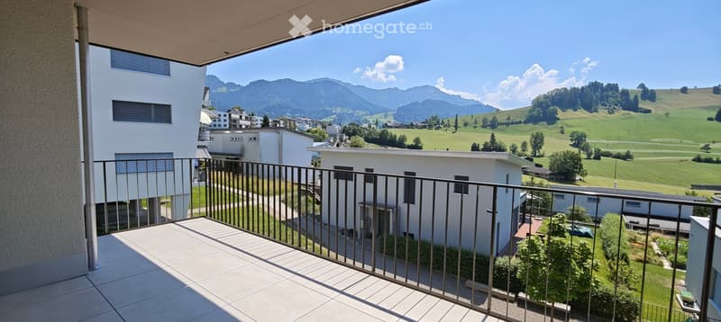 Balcony with a view of a town and surrounding mountains, featuring a metal railing and tiled floor.