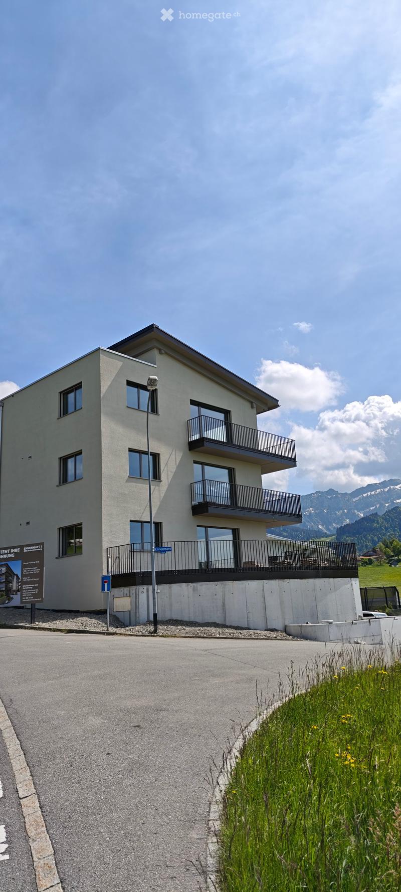 Modern two-story building with white facade, multiple windows, and balconies overlooking a scenic mountain view.