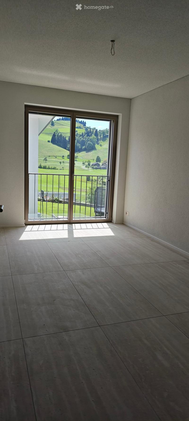 Empty room with large sliding glass door leading to a balcony, tiled floor, and scenic countryside view.