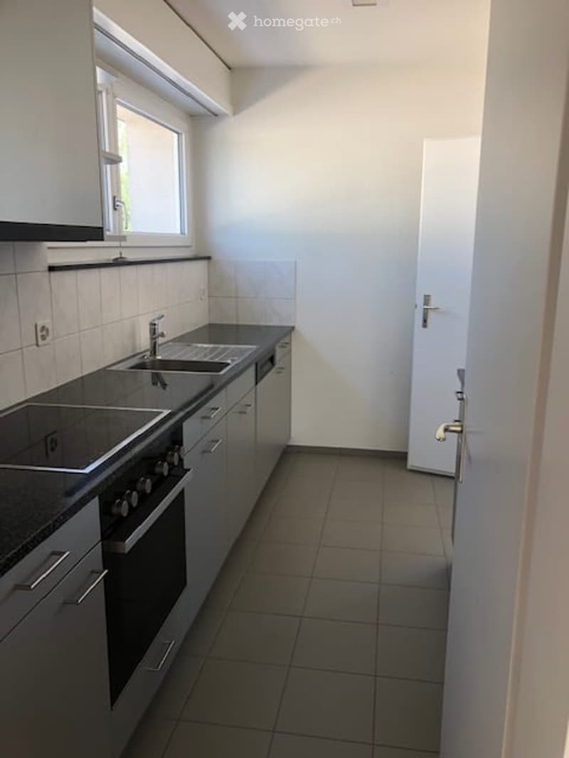 A kitchen with an oven, gas stove, double sink, cabinets, and white tiles