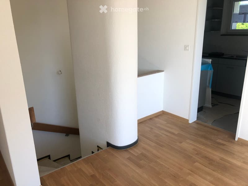Stairs, white walls, wooden floor, open door to kitchen, window