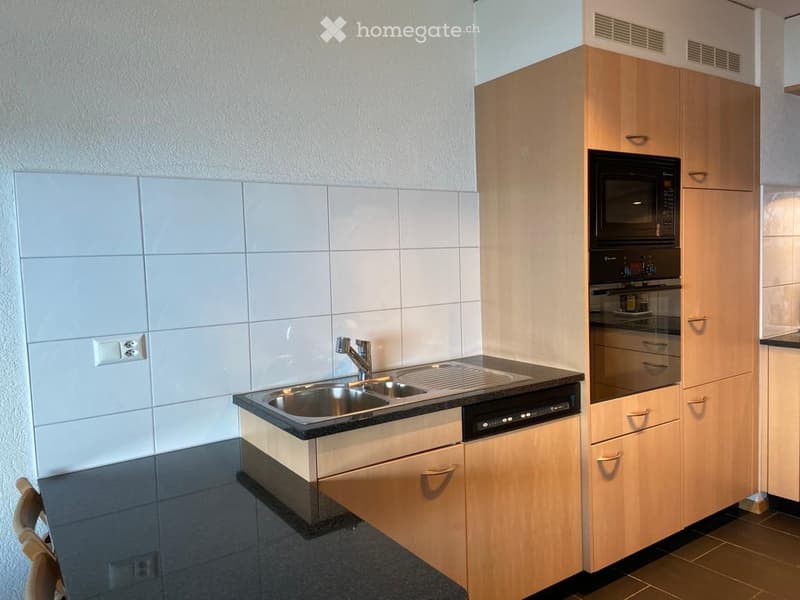 Modern kitchen with light wooden cabinets, stainless steel sink, dishwasher, and microwave. White tiled backsplash and dark countertops.